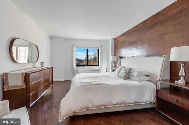 a bedroom with a bed a mirror on the dresser and a fireplace