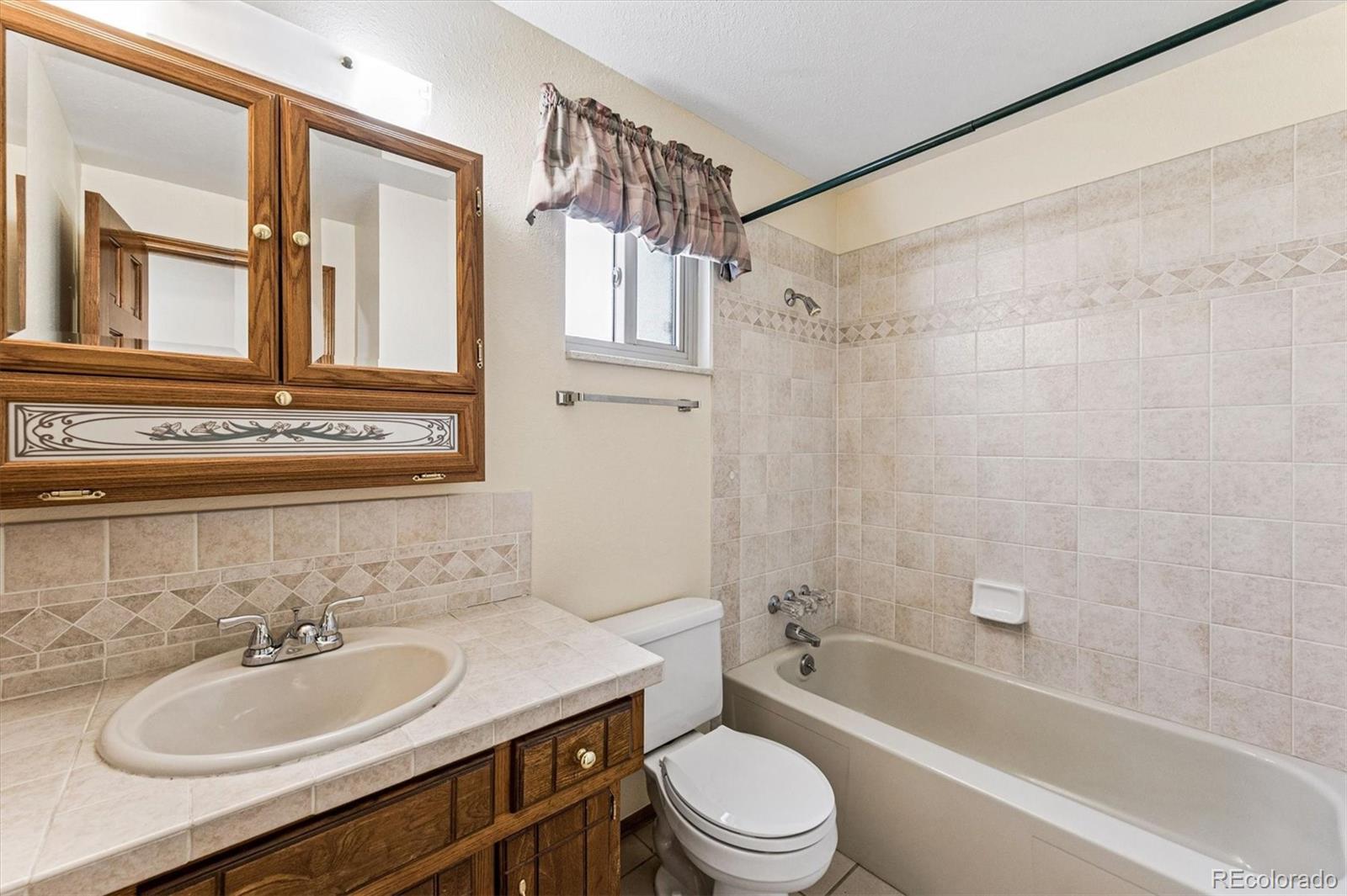 6505 West 34th Avenue Wheat Ridge, CO 80033 - Photo 16 of 28 a bathroom with a granite countertop sink toilet a mirror a bathtub and shower