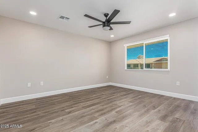 an empty room with wooden floor ceiling fan and windows