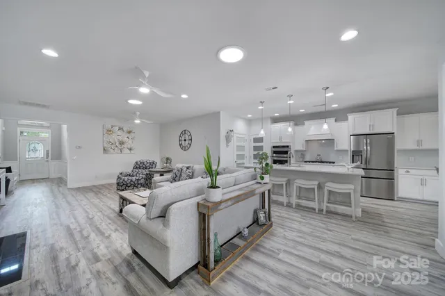 a living room with stainless steel appliances furniture wooden floor and a kitchen view