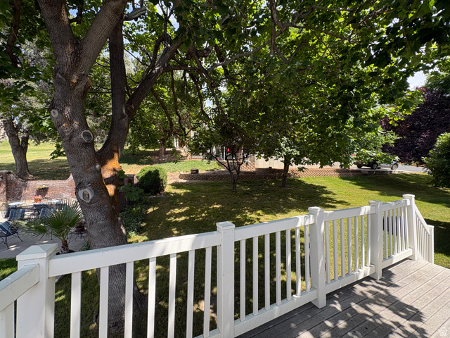 595 Meadowlark Road Orem, UT 84097 - Photo 79 of 87 Expansive outdoor space featuring a composite deck with white railings, mature trees providing natural shade, a verdant lawn, and a brick retaining wall