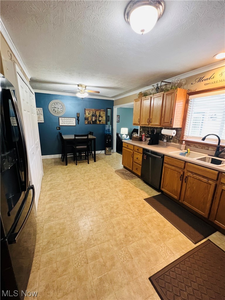 Kitchen with black appliances, a textured ceiling, brown cabinets, light countertops, ornamental molding, and light tile floors