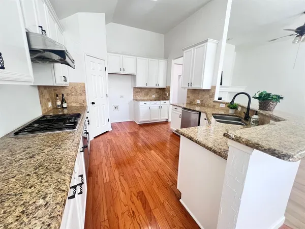 a large kitchen with granite countertop a stove top oven a sink a dishwasher and white cabinets with wooden floor