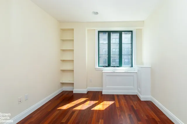 a view of an empty room with wooden floor and a window