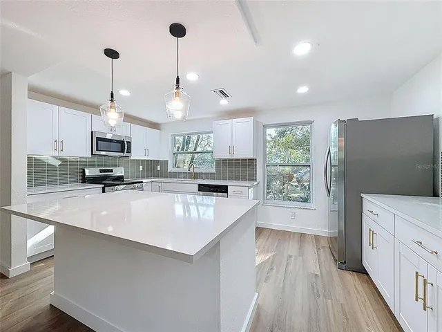 a large kitchen with stainless steel appliances a large counter top a stove a sink dishwasher a refrigerator and a fireplace with wooden floor