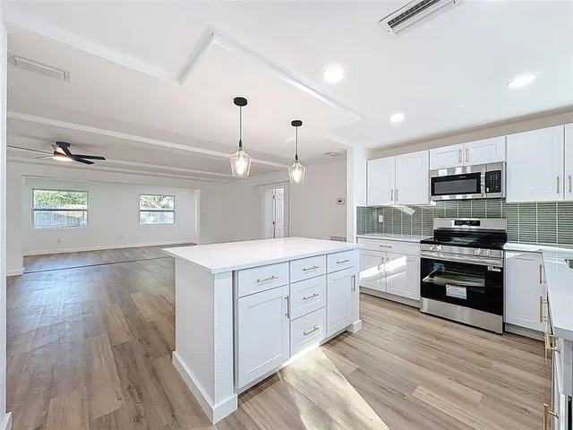 a kitchen with stainless steel appliances a stove top oven a sink dishwasher a refrigerator and a dining table with wooden floor