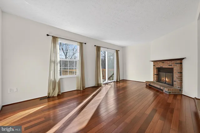 a view of an empty room with wooden floor fireplace and a window