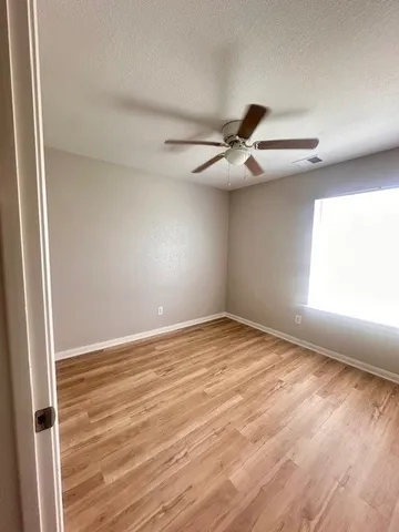 an empty room with wooden floor fan and windows