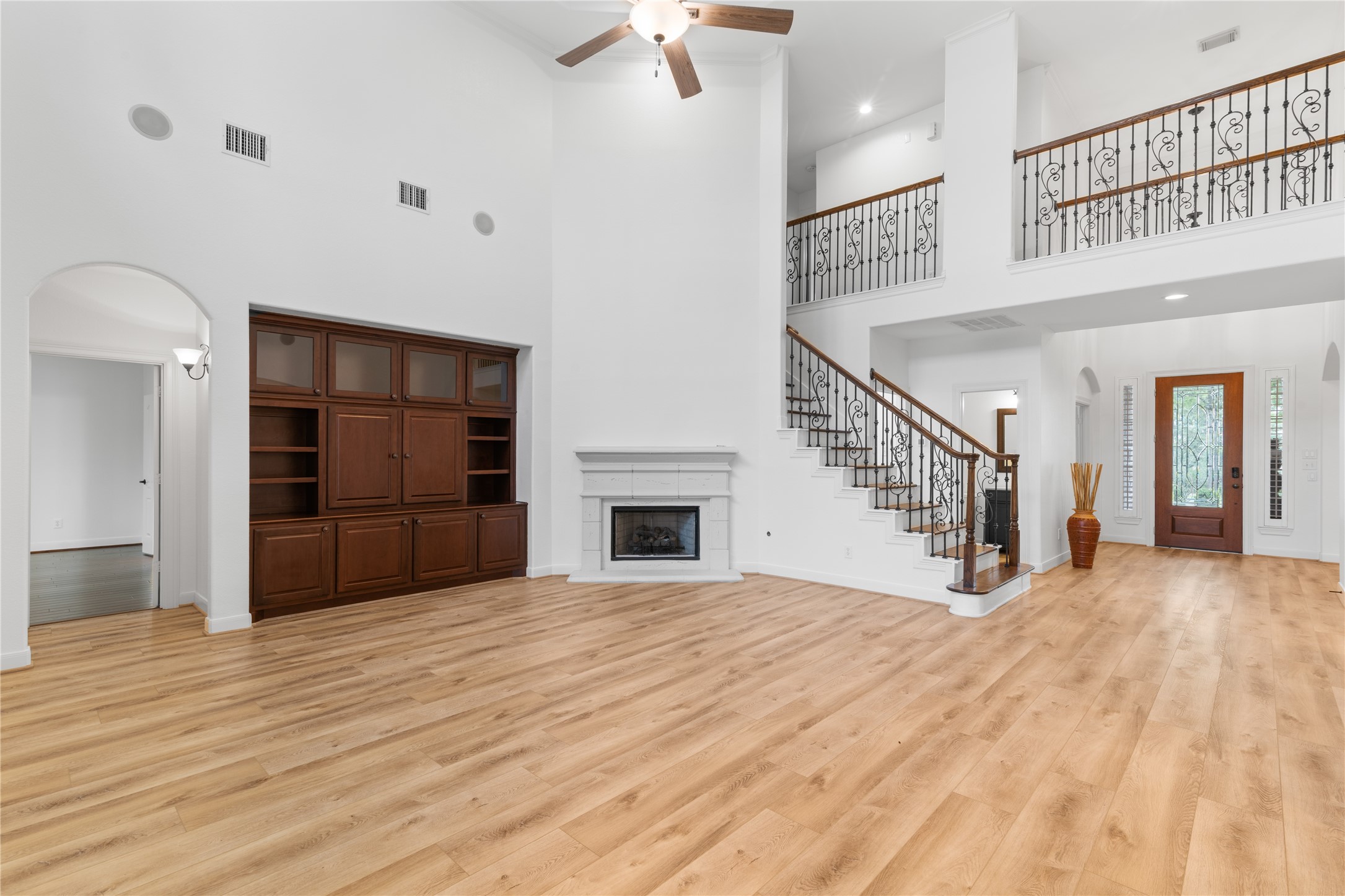 155 South Arrow Canyon Circle Spring, TX 77389 - Photo 16 of 49 This spacious family room with high ceilings is adorned by a cozy fireplace and built-in shelving. The elegant staircase with wrought-iron railing leads to an upper level, adding charm. The well-lit gathering room opens to the hallway to the front door, offering a distinctive and inviting atmosphere.