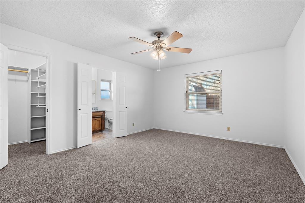 921 Red Oak Street Azle, TX 76020 - Photo 11 of 16 Primary bedroom featuring carpet flooring, connected bathroom, a textured ceiling, a spacious closet, and ceiling fan