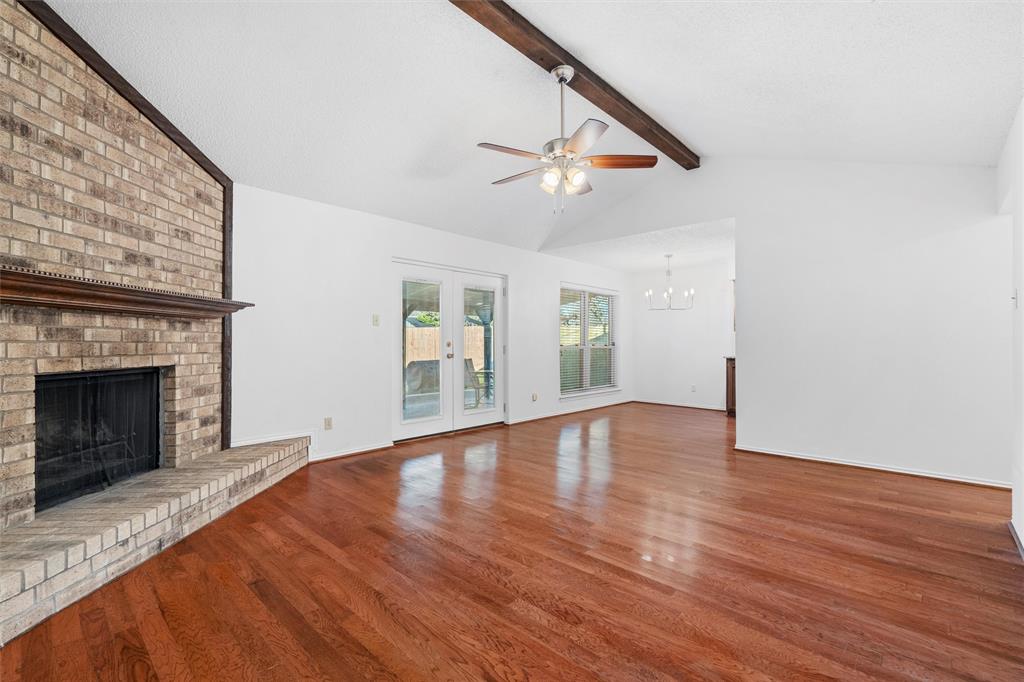 921 Red Oak Street Azle, TX 76020 - Photo 3 of 16 Unfurnished living room featuring dark wood-style floors, a brick fireplace, ceiling fan, beamed ceiling, and suspended lighting