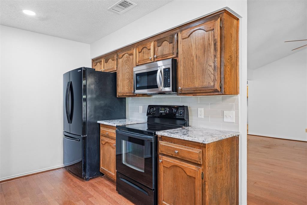 921 Red Oak Street Azle, TX 76020 - Photo 8 of 16 Kitchen featuring black appliances, light wood-style floors, wood finish cabinets, decorative backsplash, and light stone countertops