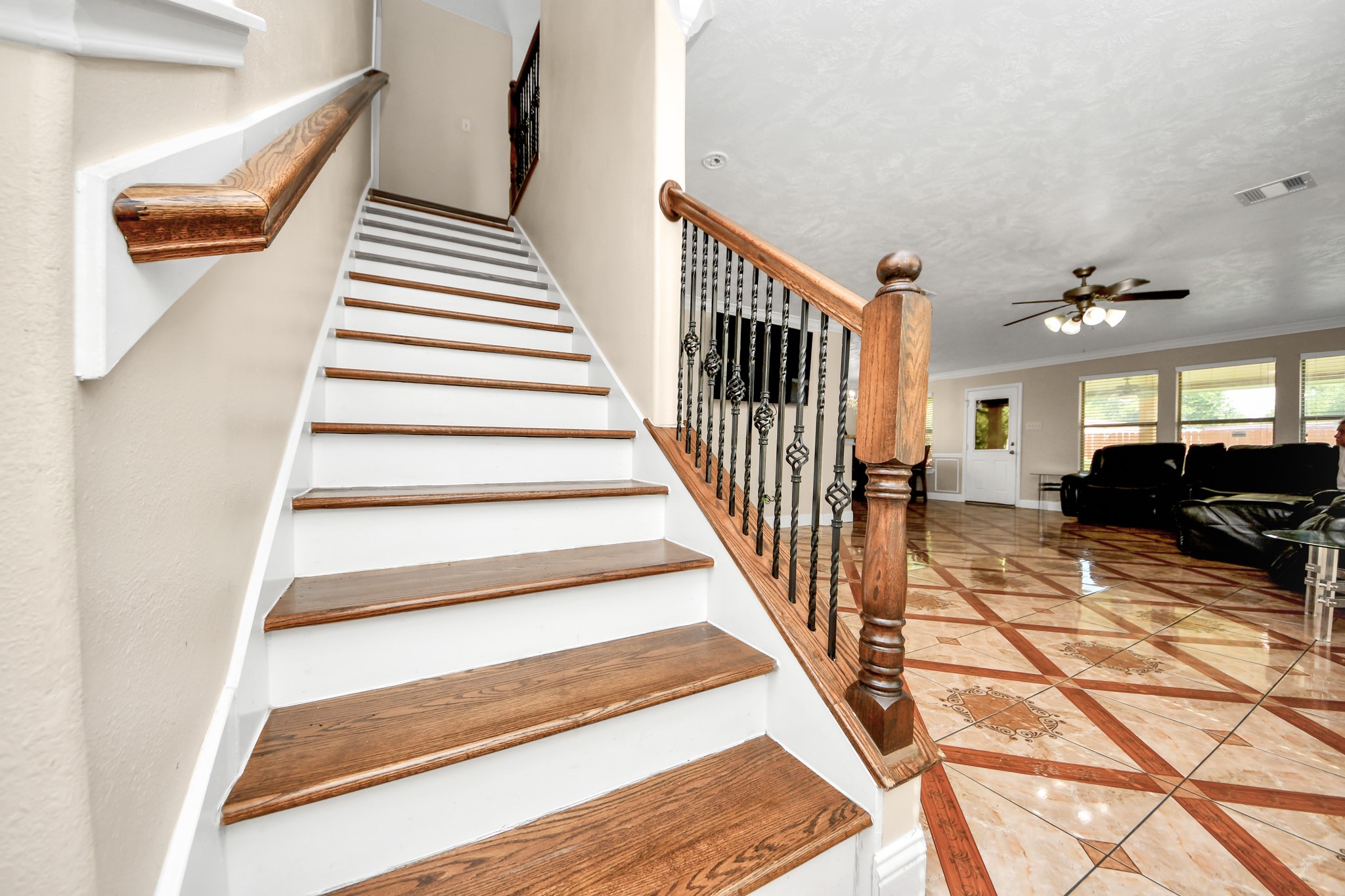 9250 Strawberry Cactus Loop Houston, TX 77064 - Photo 14 of 26 Elegant staircase with rich wood accents leads to a spacious, bright living area featuring glossy tiled floors and a cozy seating arrangement.