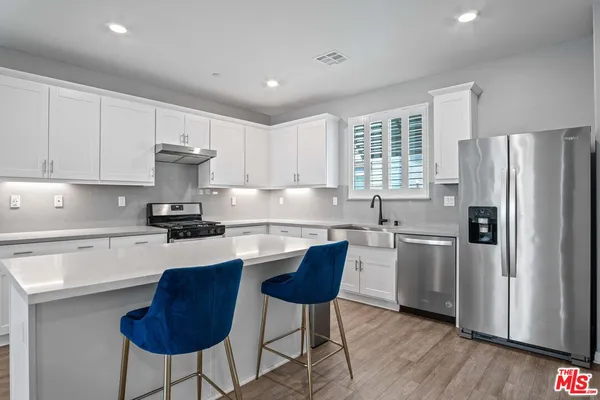 a kitchen with stainless steel appliances granite countertop a refrigerator a stove a sink cabinets and a dining table with wooden floor