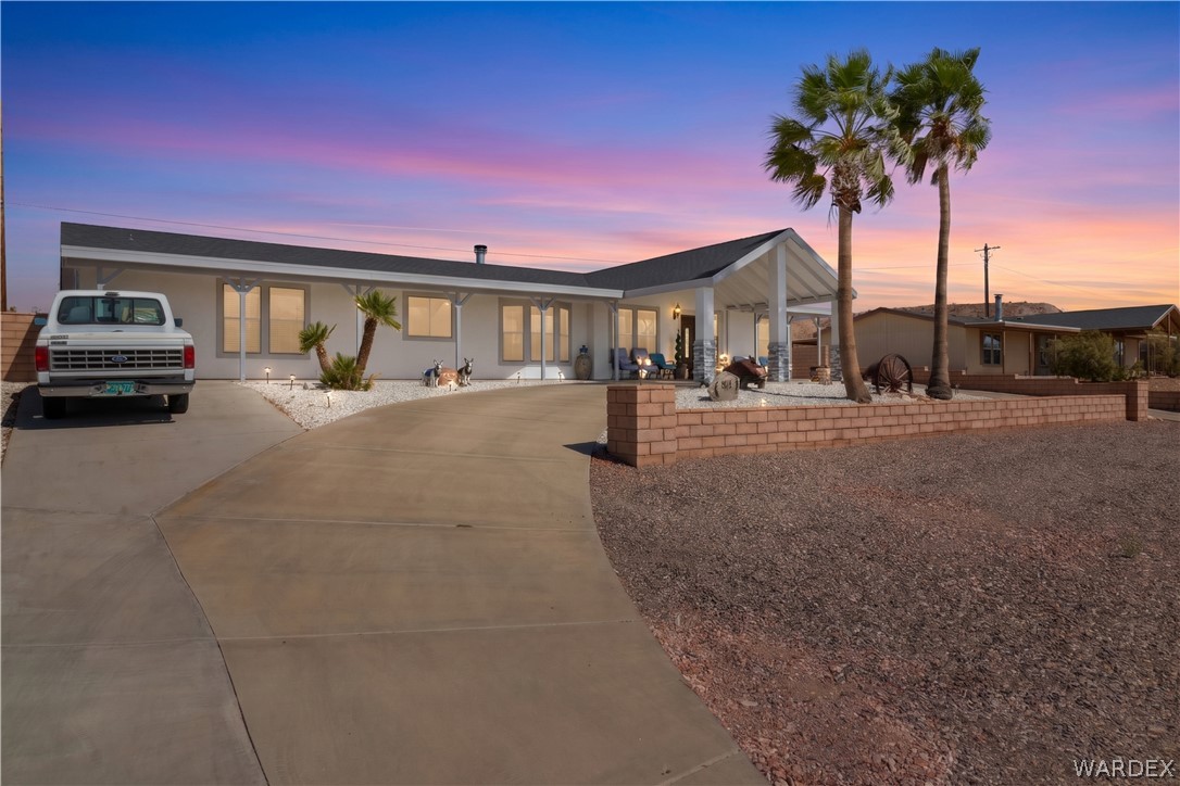 784 Pegasus Ranch Road Bullhead City, AZ 86429 - Photo 2 of 100 Single-story residence featuring a covered front entry, concrete driveway, and desert landscaping with palm trees