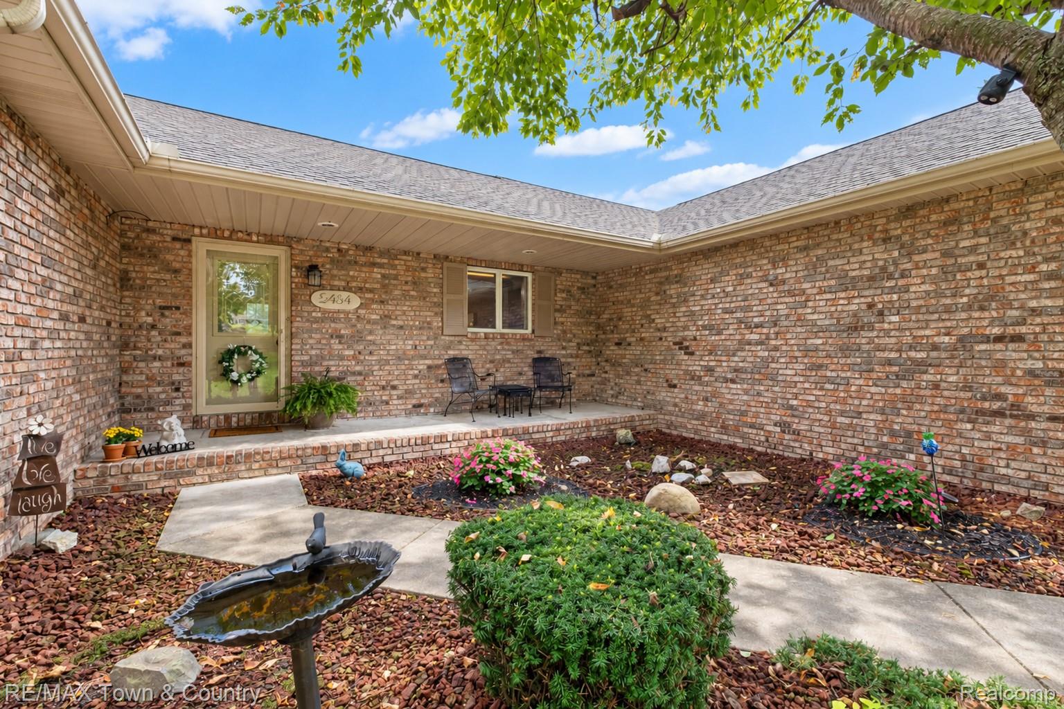 5464 North Seymour Road Flushing, MI 48433 - Photo 6 of 45 Brick exterior featuring a covered porch, established shrubbery, and a concrete walkway