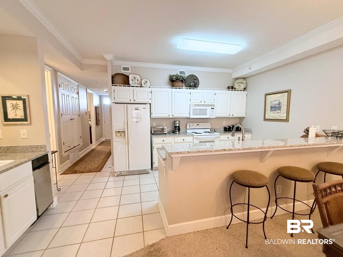 27284 Gulf Road, Unit 212 Orange Beach, AL 36561 - Photo 7 of 35 Kitchen featuring a breakfast bar area, white cabinets, light stone counters, white appliances, and crown molding
