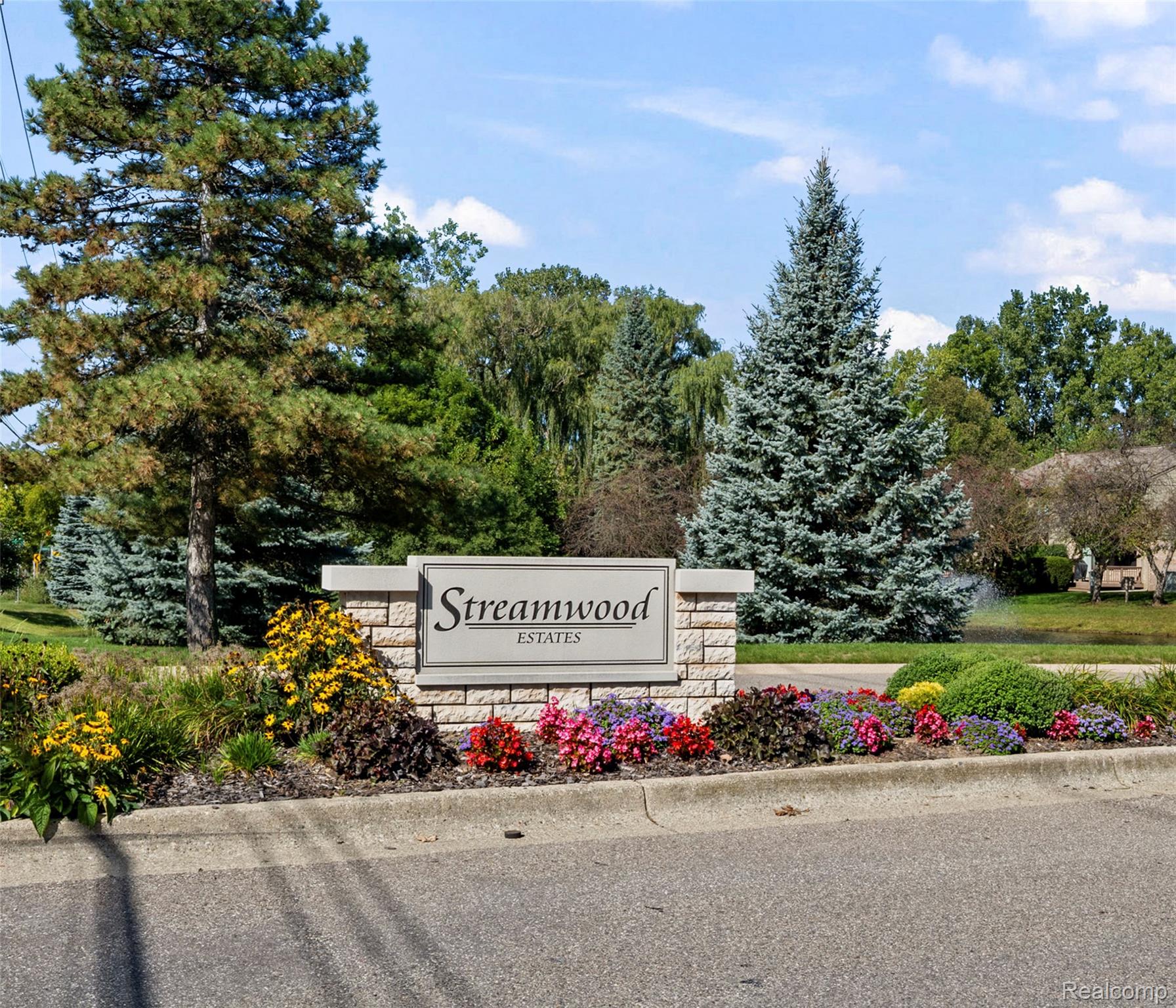 1830 Streamedge Court Rochester, MI 48309 - Photo 27 of 33 Stone-clad community signage featuring a framed nameplate, surrounded by mature trees and vibrant landscaping