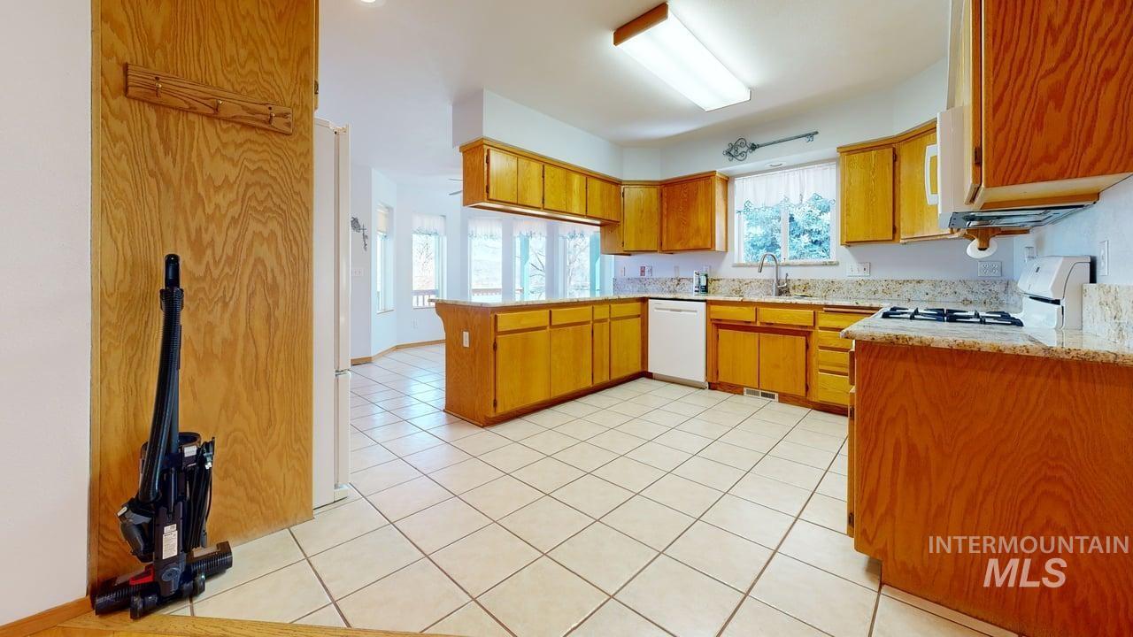 2794 9th Avenue Clarkston, WA 99403 - Photo 4 of 34 Kitchen featuring a peninsula, white appliances, wood finish cabinetry, light tile patterned floors, and light stone countertops