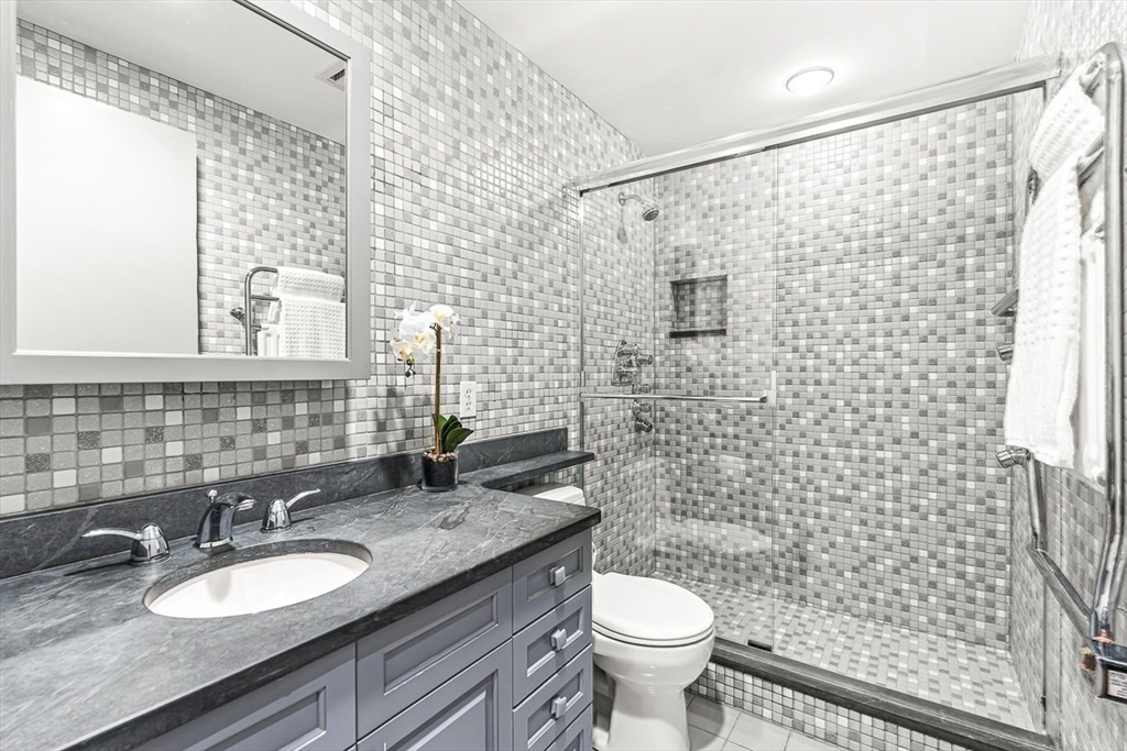 67 Algonquin Road, Unit 67 Newton, MA 02467 - Photo 32 of 38 a bathroom with a granite countertop toilet a sink a mirror and shower curtain