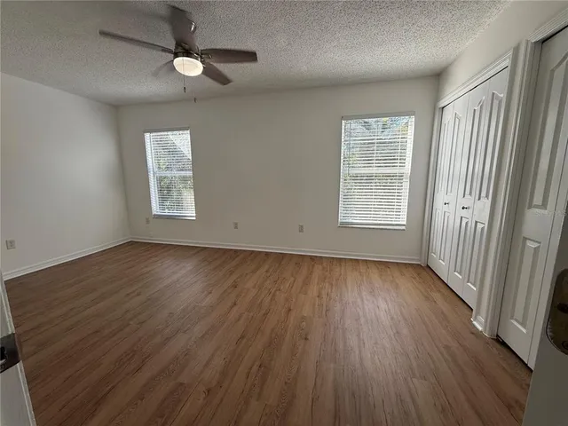an empty room with wooden floor chandelier fan and windows