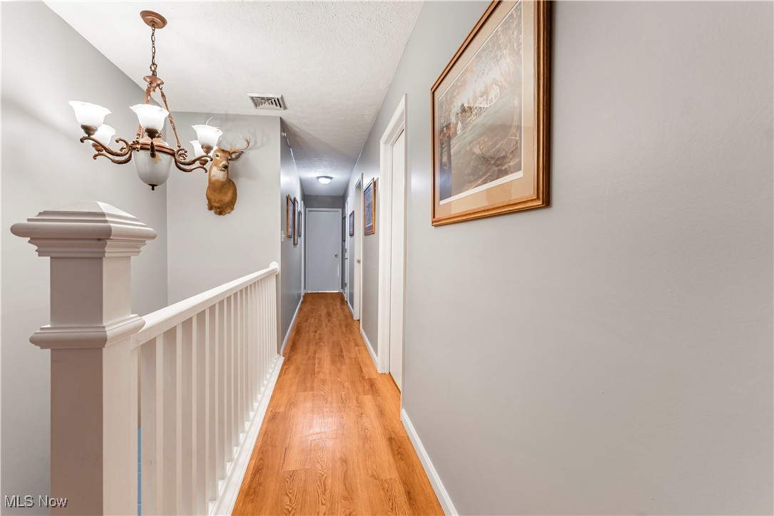 155 Ridgewood Boulevard Belpre, OH 45714 - Photo 34 of 49 Hallway featuring light wood-type flooring, a chandelier, a textured ceiling, and an upstairs landing