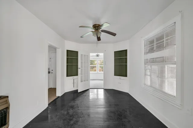 an empty room with chandelier fan and windows