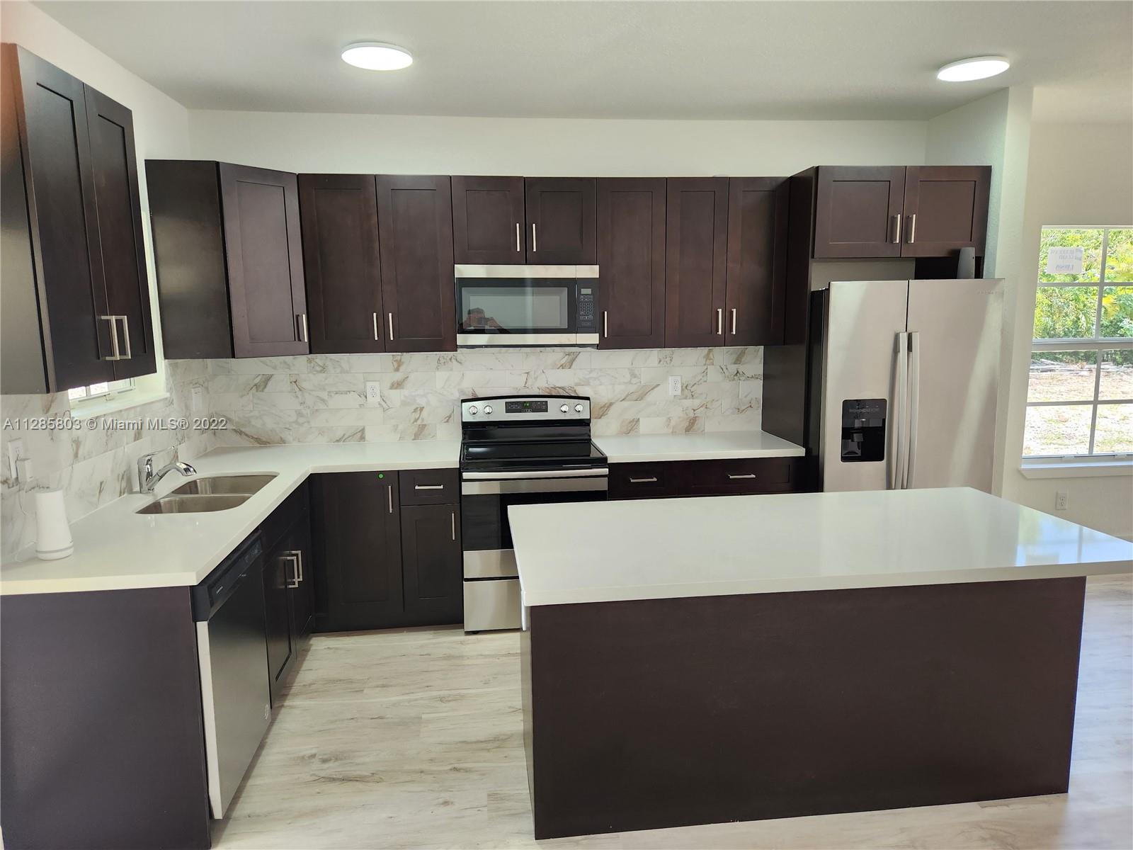 22065 Miami Avenue Miami, FL 33170 - Photo 10 of 27 a kitchen with kitchen island granite countertop a refrigerator stove a sink and dishwasher with wooden cabinet