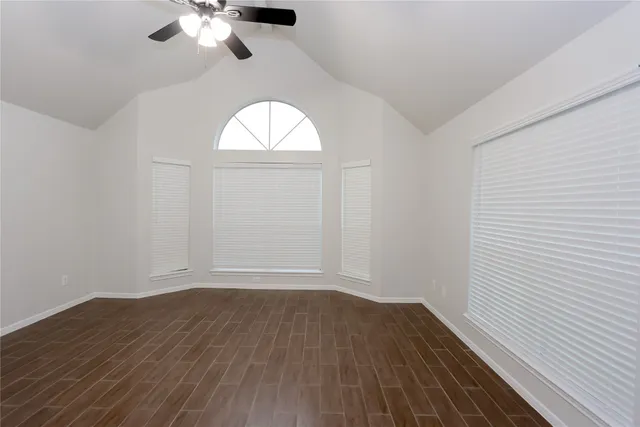 an empty room with wooden floor chandelier fan and windows
