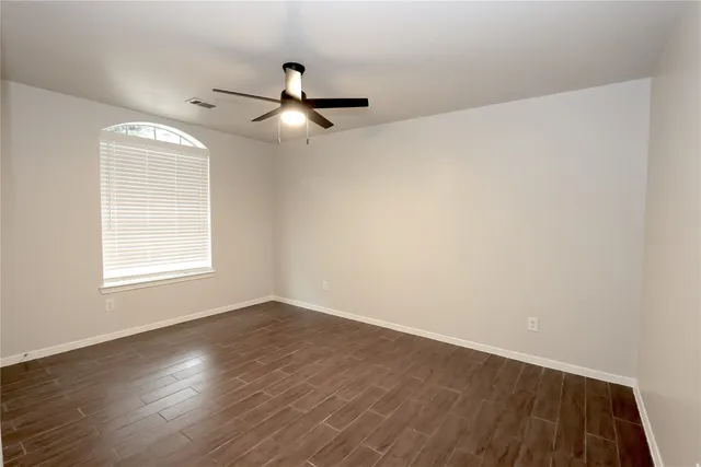 an empty room with wooden floor ceiling fan and windows
