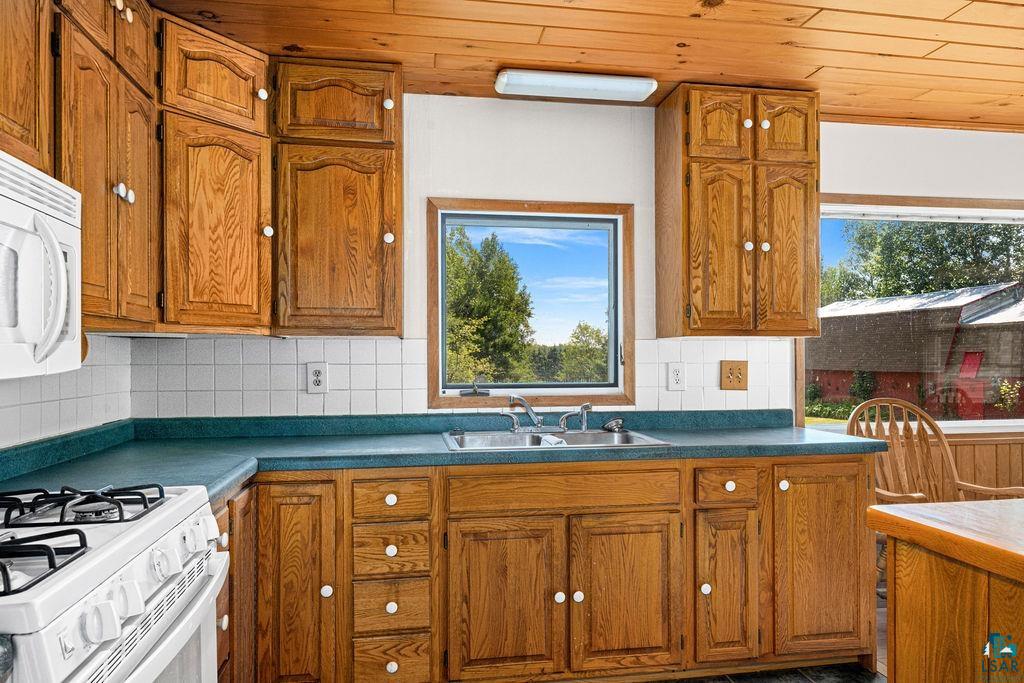 2592 Strandberg Road Barnum, MN 55707 - Photo 7 of 44 Kitchen featuring wood-finish cabinetry, a white tile backsplash, an integrated double-basin sink, and a large window overlooking exterior scenery