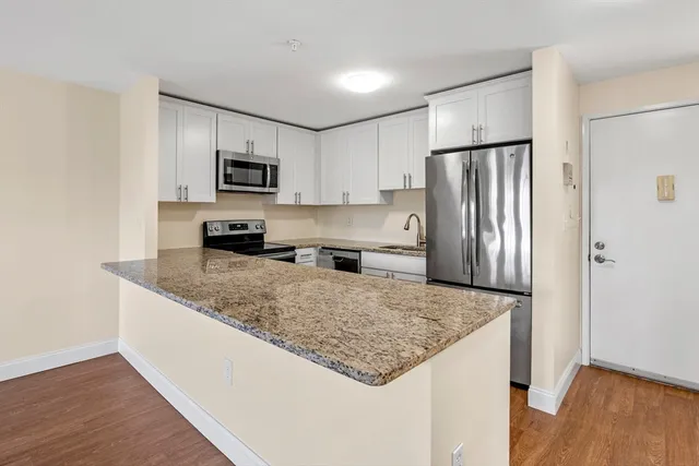 a kitchen with stainless steel appliances granite countertop a refrigerator a stove and a sink with wooden floor