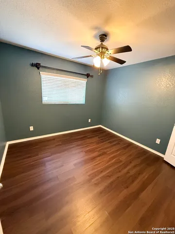 a view of an empty room with wooden floor and a ceiling fan