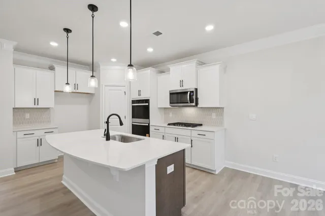 a kitchen with stainless steel appliances granite countertop a sink a stove a refrigerator and white cabinets with wooden floor