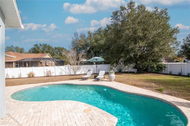 a view of pool with lawn chairs and large trees