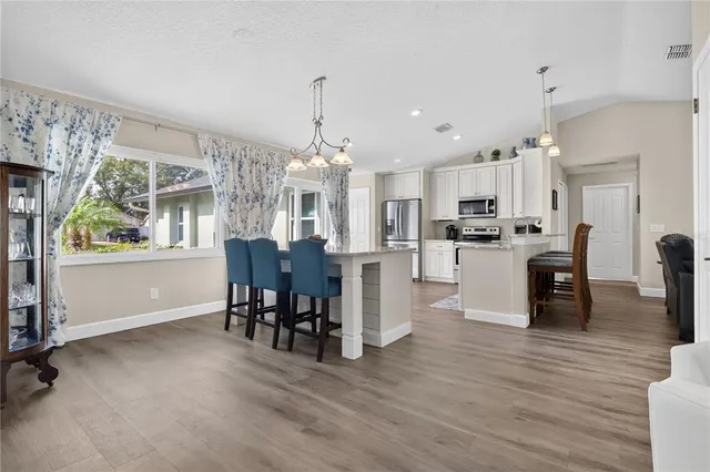 a open kitchen with stainless steel appliances granite countertop a refrigerator dining table and chairs with wooden floor