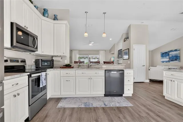 a kitchen with stainless steel appliances granite countertop a refrigerator a stove top oven a sink dishwasher and white cabinets with wooden floor