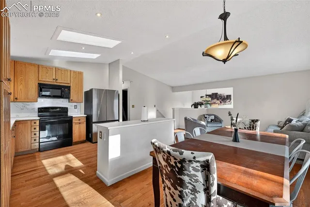 a kitchen with stainless steel appliances granite countertop a refrigerator a sink dishwasher a dining table and chairs with wooden floor