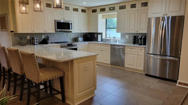 a kitchen with stainless steel appliances granite countertop a stove a sink a microwave a refrigerator and white cabinets