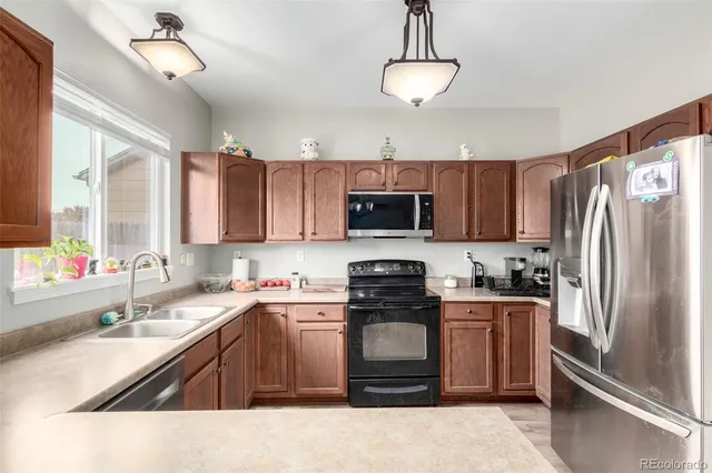 a kitchen with stainless steel appliances granite countertop a sink a stove a refrigerator cabinets a window and a couch