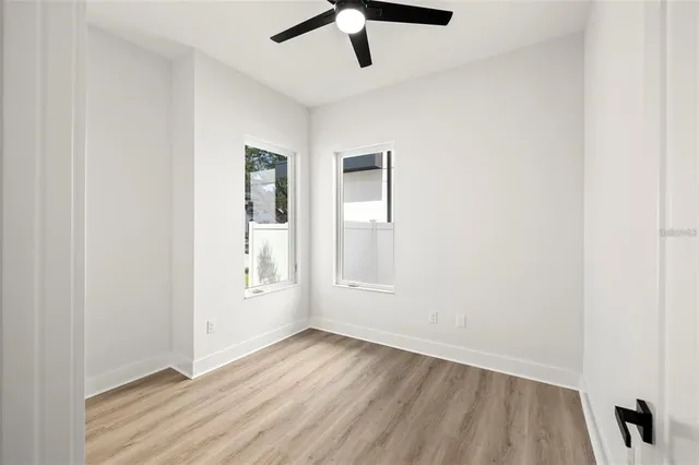 an empty room with wooden floor ceiling fan and windows