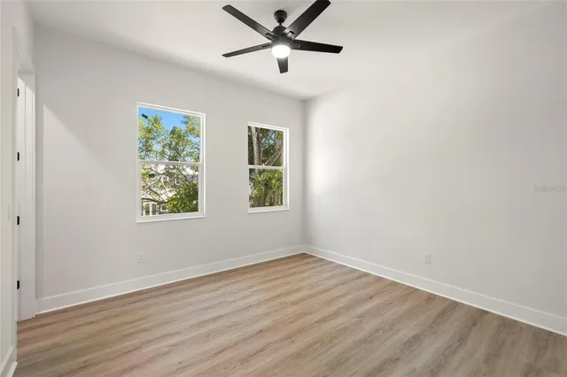 a view of a room with wooden floor a ceiling fan and windows