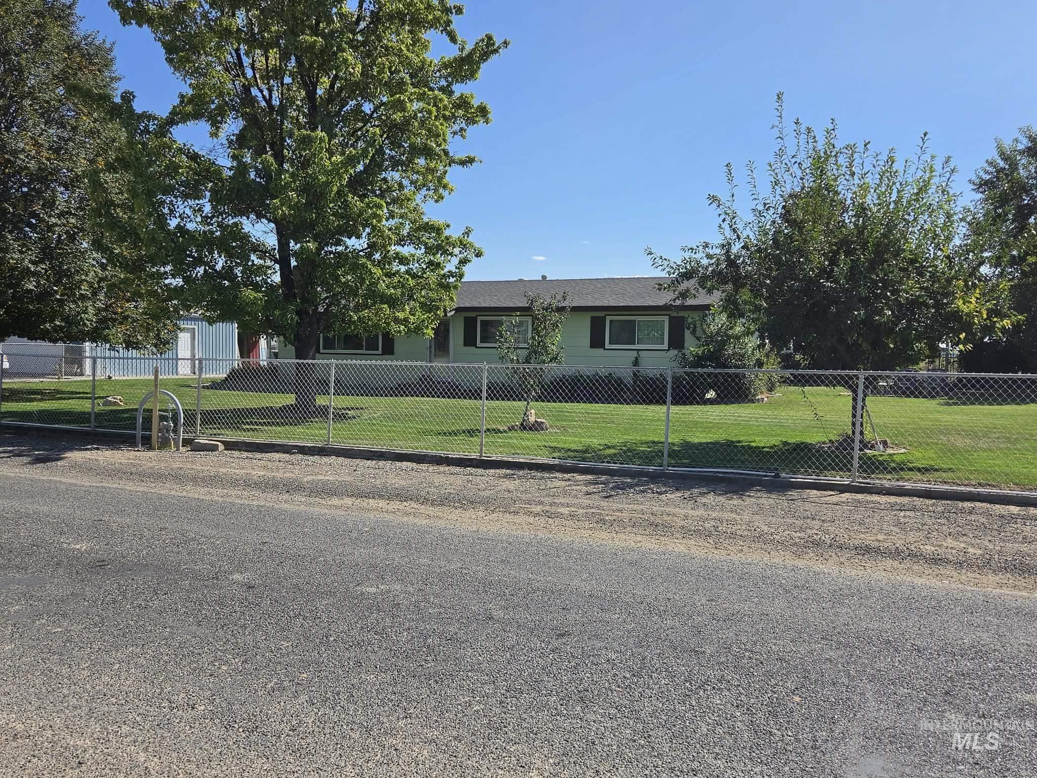 Chain-link perimeter fencing enclosing a manicured lawn, mature trees, and a single-story residence with dark window shutters