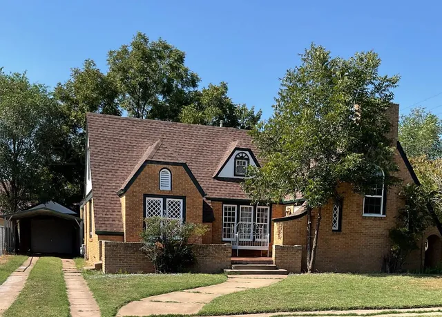 a view of a house with a yard plants and large tree
