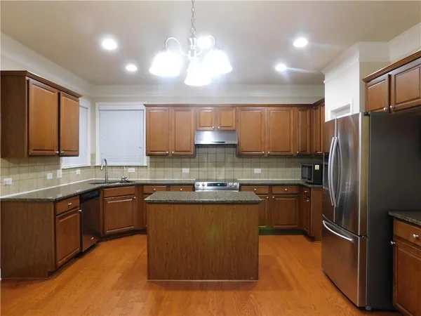 a kitchen with stainless steel appliances granite countertop wooden cabinets a refrigerator a sink a stove a kitchen island and cabinets