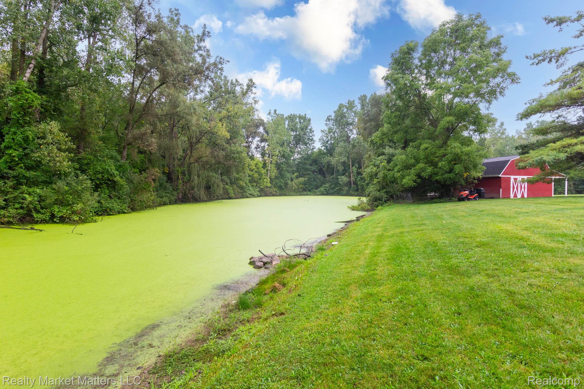 770 North Fairgrounds Road Imlay City, MI 48444 - Photo 42 of 55 Expansive green space featuring a red barn structure with white trim, a verdant pond, and mature trees outlining the property