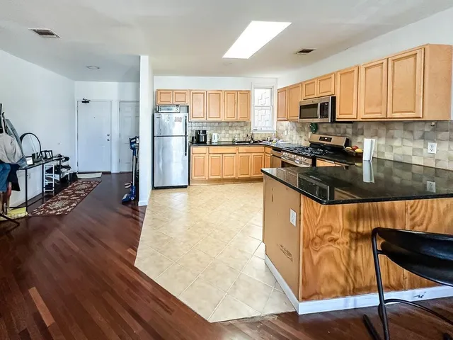 a kitchen with stainless steel appliances granite countertop wooden cabinets a refrigerator a stove a sink and a microwave oven with wooden floor