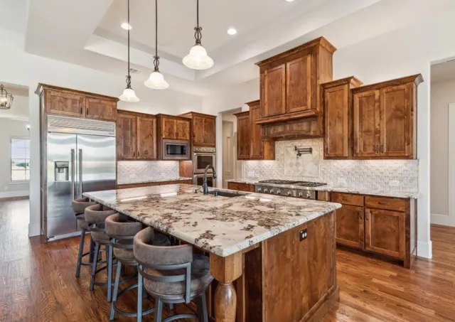 a kitchen with a stove a refrigerator a oven a sink with island chairs and wooden floor