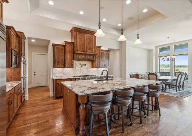 a kitchen with stainless steel appliances kitchen island granite countertop a table chairs sink and wooden floor