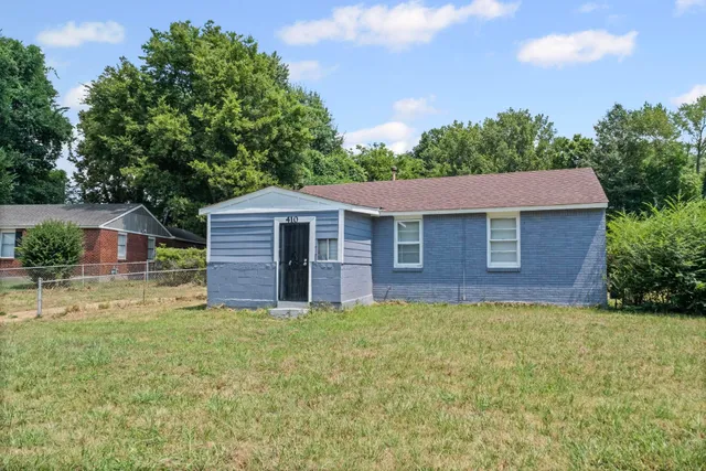 a brick house with a big yard and large trees